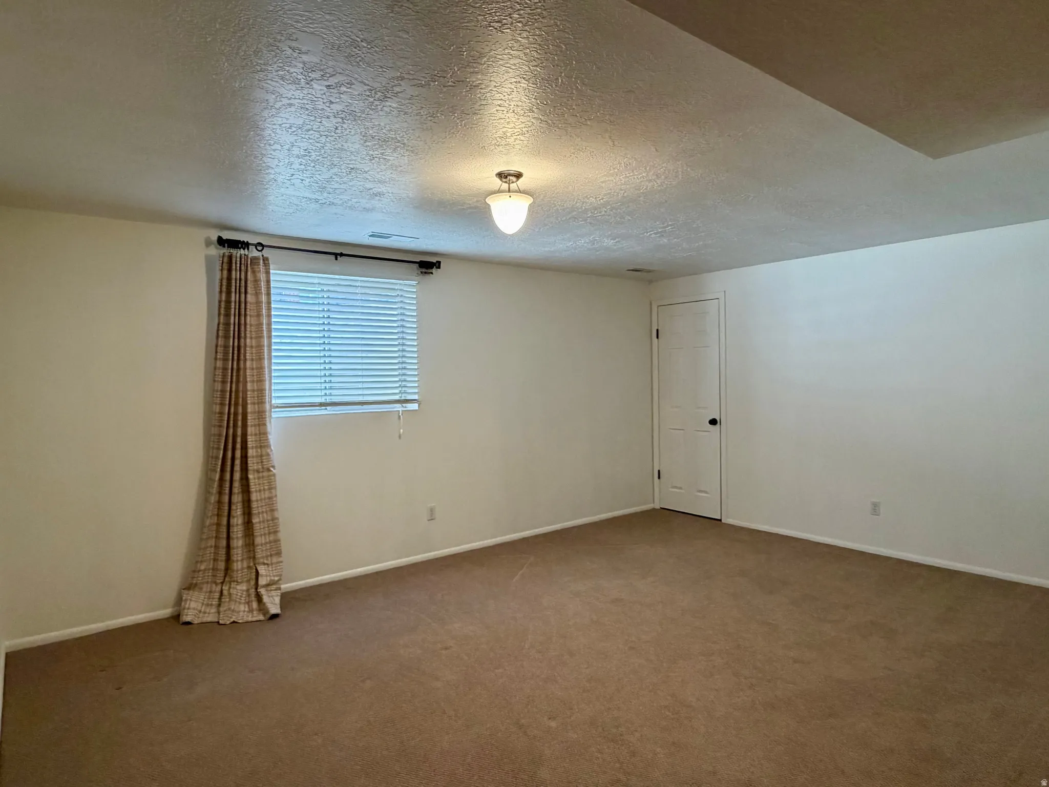 Carpeted empty room featuring a textured ceiling and baseboards