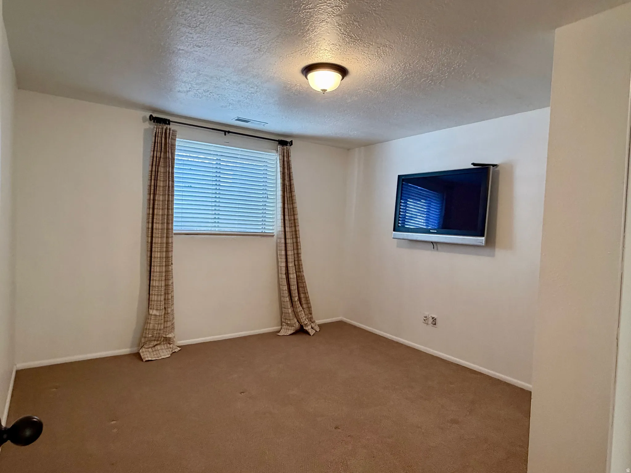 Carpeted empty room with a textured ceiling and baseboards
