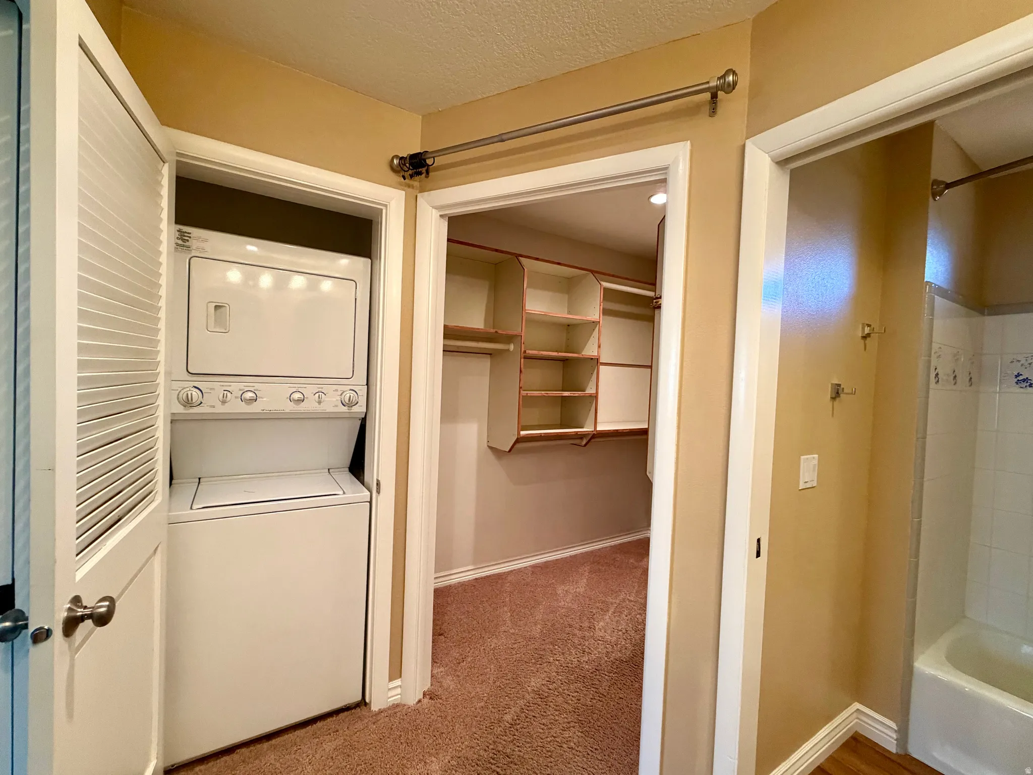 Laundry area with stacked washer / dryer, light carpet, and a textured ceiling