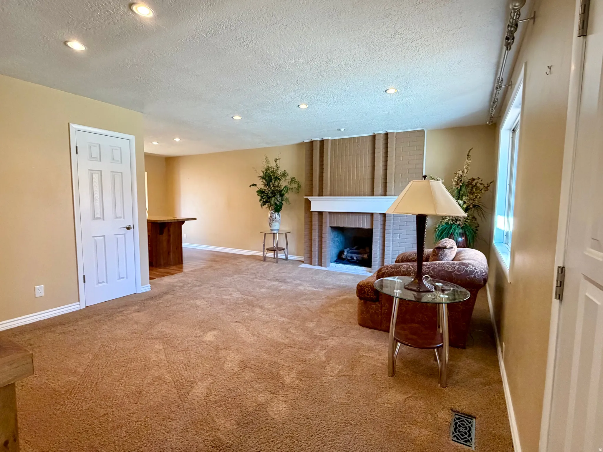 Living area featuring a brick fireplace, recessed lighting, light carpet, and a textured ceiling