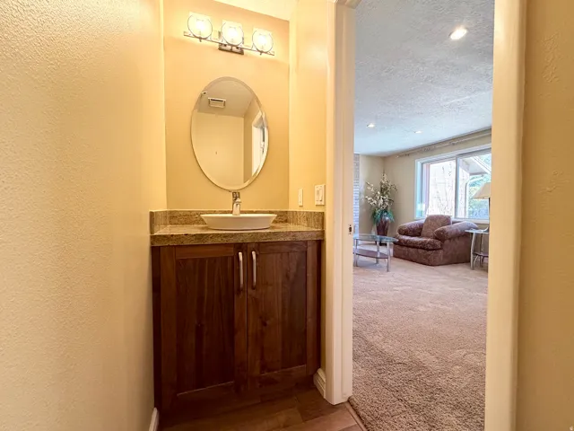 Half bathroom featuring vanity, toilet, a textured wall, a textured ceiling, dark colored carpet, and recessed lighting