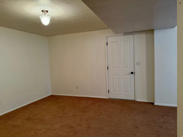 Carpeted spare room with a textured ceiling and baseboards