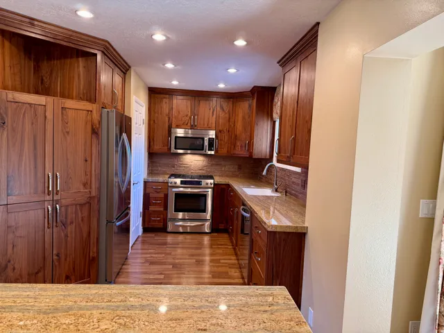 Kitchen with stainless steel appliances, light stone countertops, light wood-type flooring, backsplash, and brown cabinetry