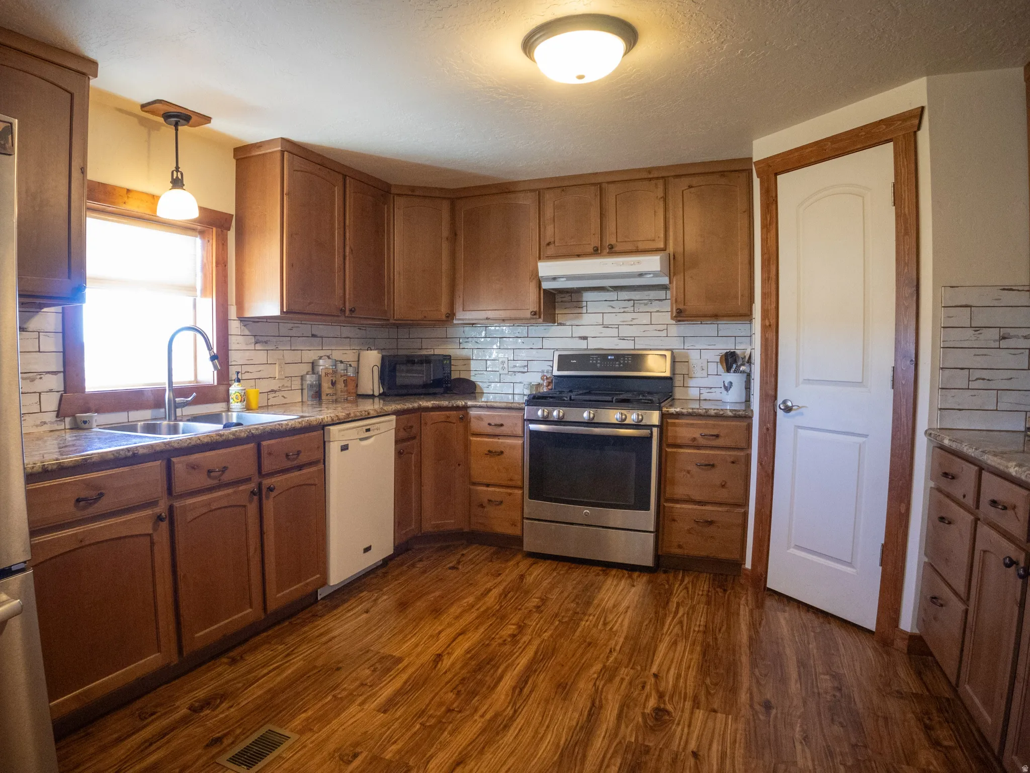 Kitchen featuring stainless steel appliances, decorative light fixtures, light stone countertops, dark wood-style flooring, and a textured ceiling
