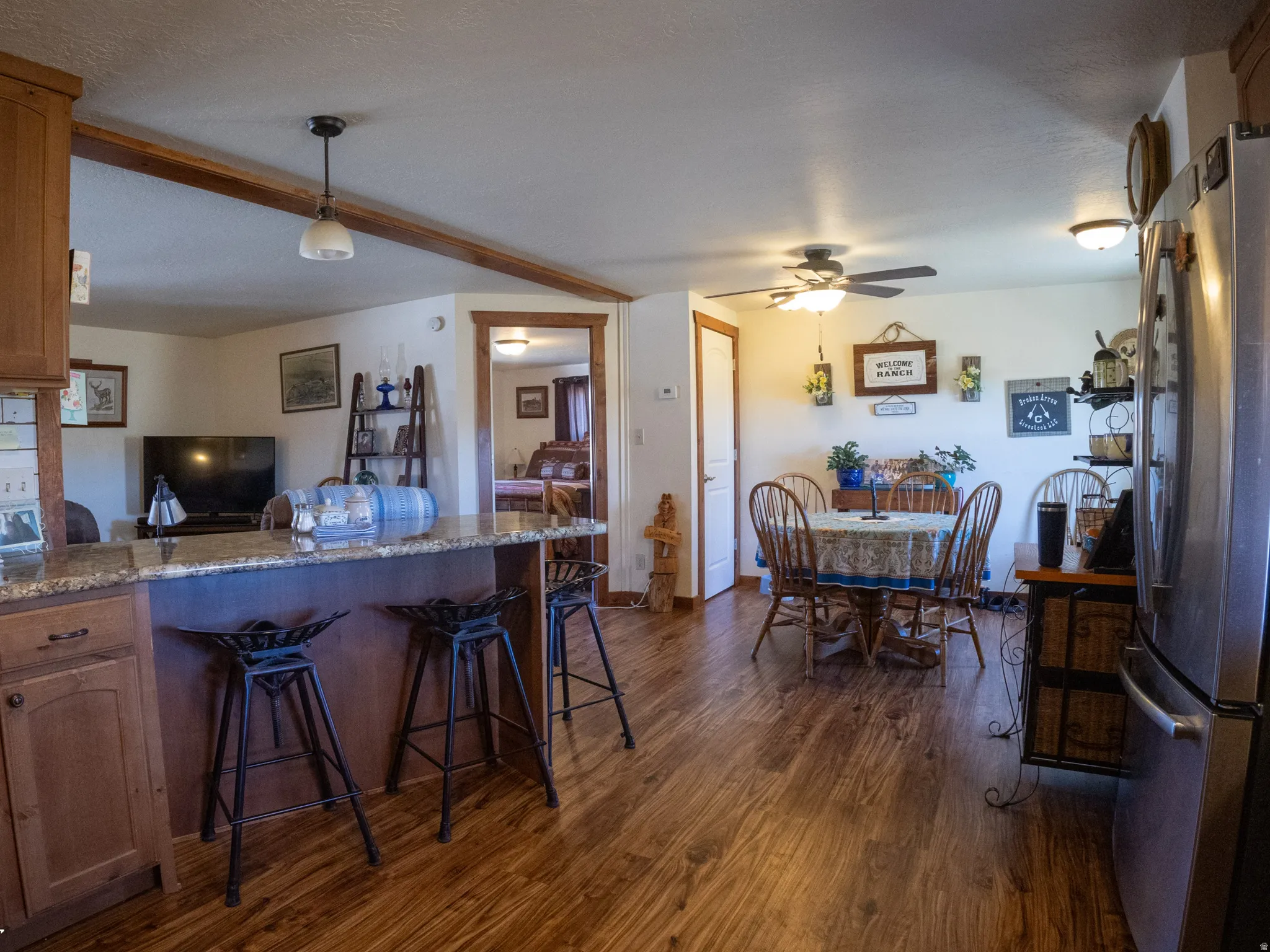 Kitchen with dark stone counters, freestanding refrigerator, brown cabinetry, a peninsula, and dark wood-type flooring
