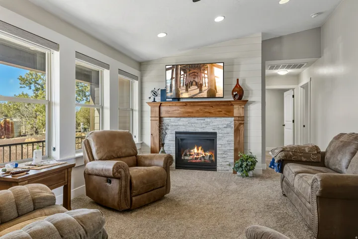Living room with vaulted ceiling, a stone fireplace, carpet floors, and recessed lighting