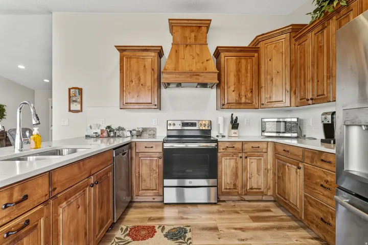 Kitchen with appliances with stainless steel finishes, premium range hood, brown cabinetry, light wood-style flooring, and backsplash