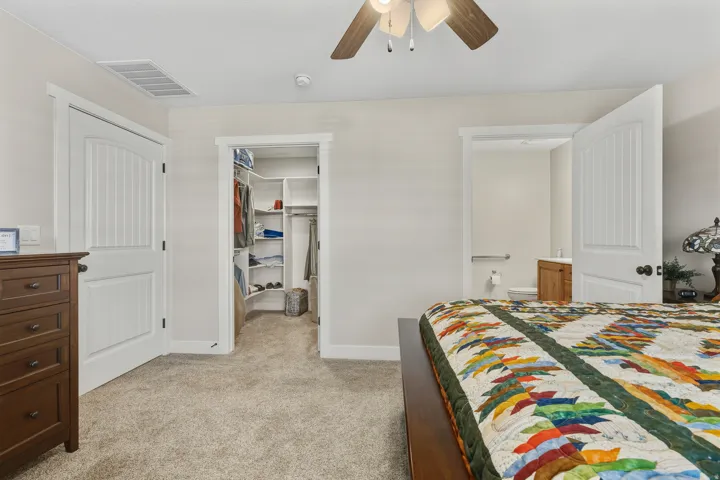 Bedroom with light carpet, a walk in closet, ceiling fan, and ensuite bathroom