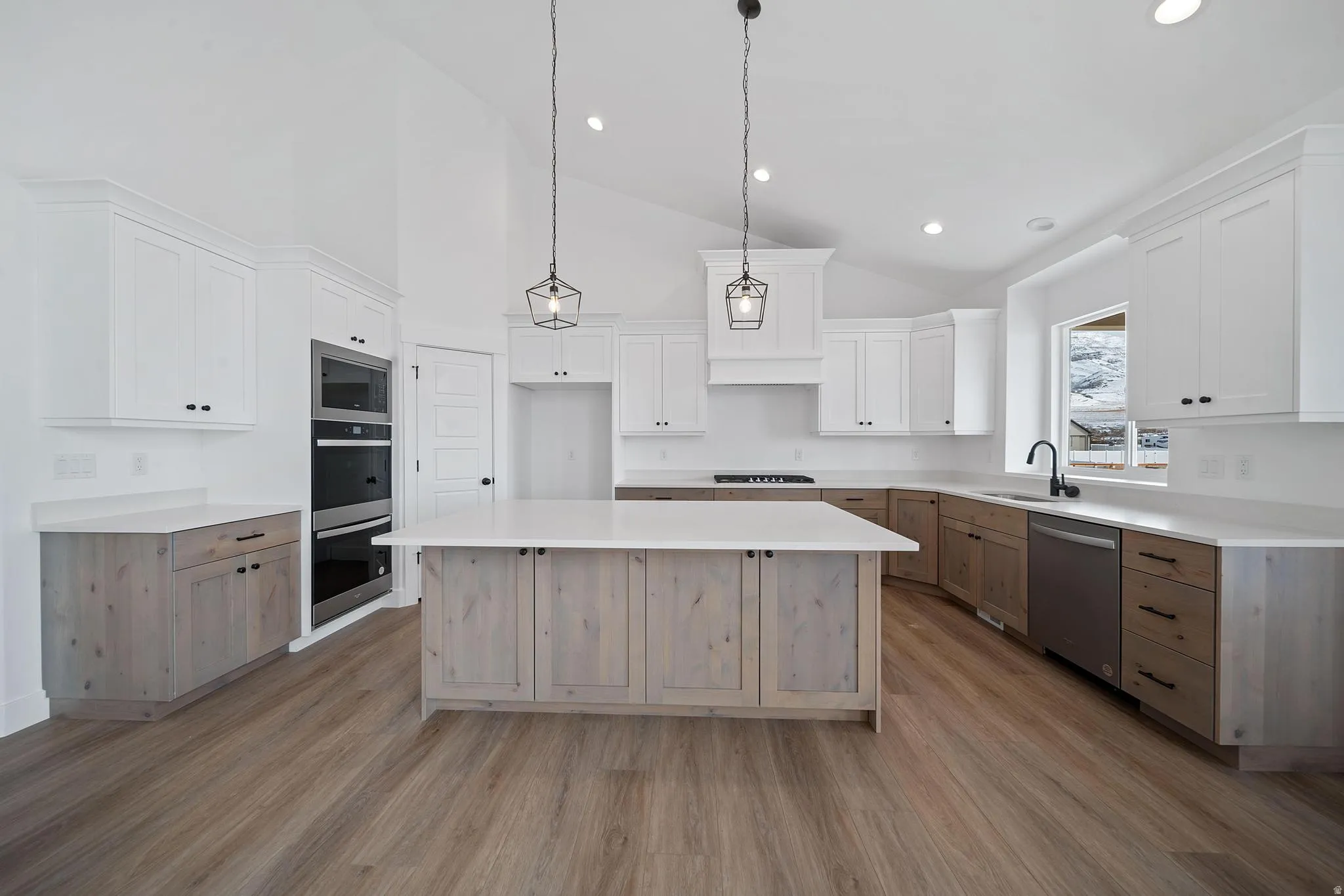 Kitchen with white cabinetry, a kitchen island, hanging light fixtures, appliances with stainless steel finishes, and high vaulted ceiling