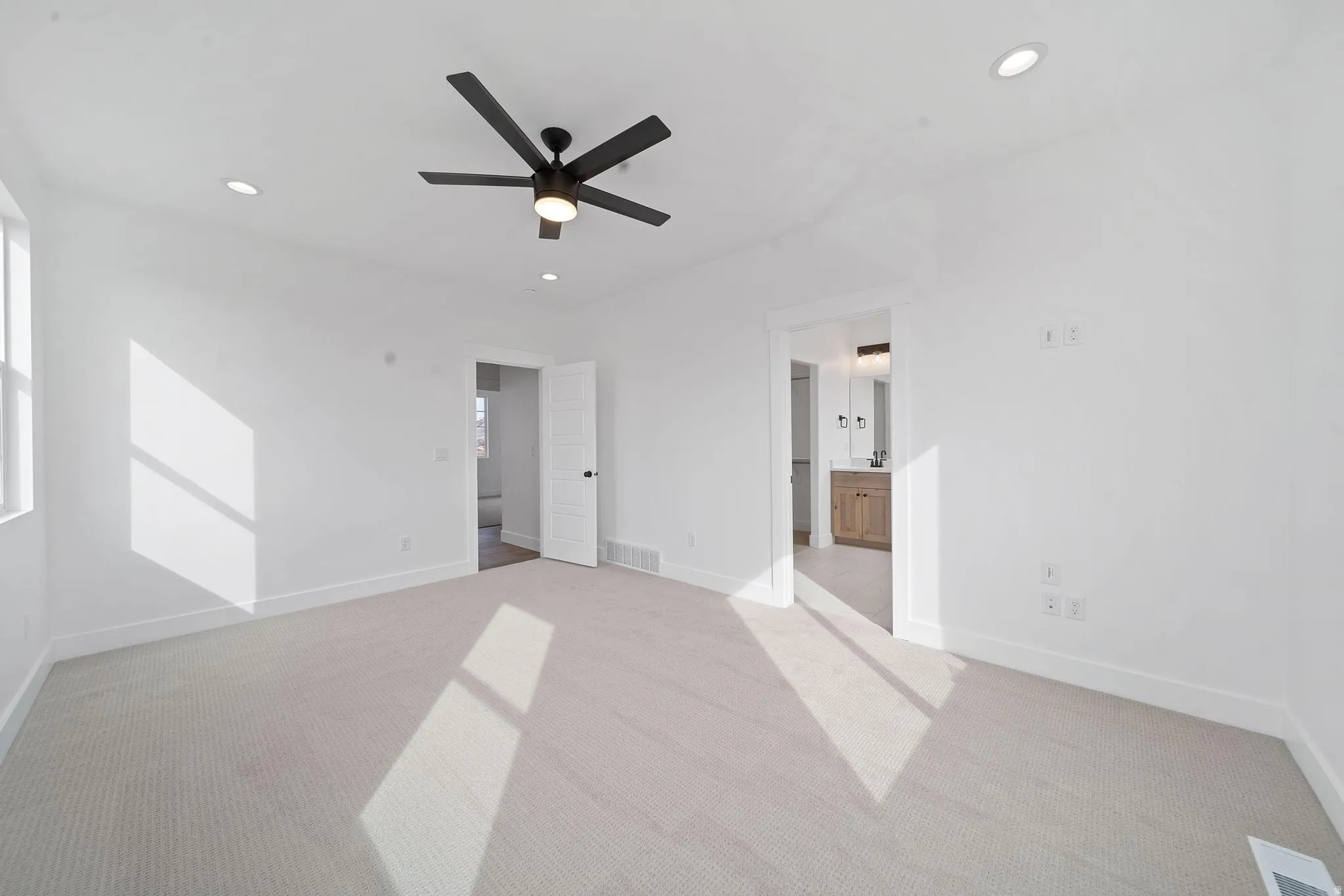 Unfurnished bedroom with light carpet, ceiling fan, ensuite bathroom, and recessed lighting