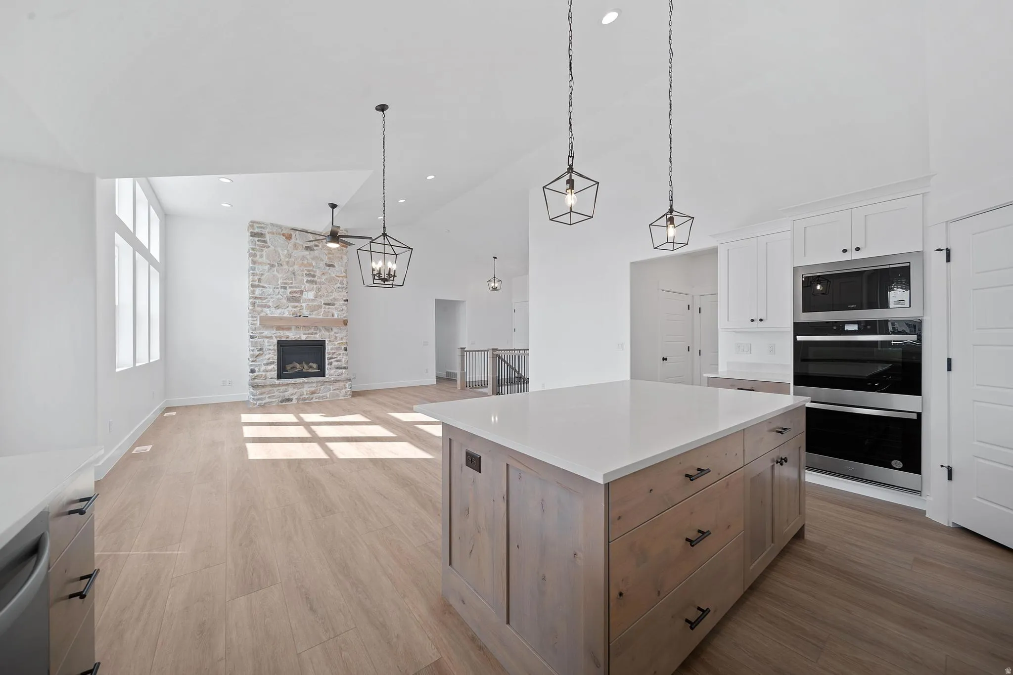 Kitchen featuring high vaulted ceiling, light wood-style flooring, stainless steel appliances, a stone fireplace, and light brown cabinetry