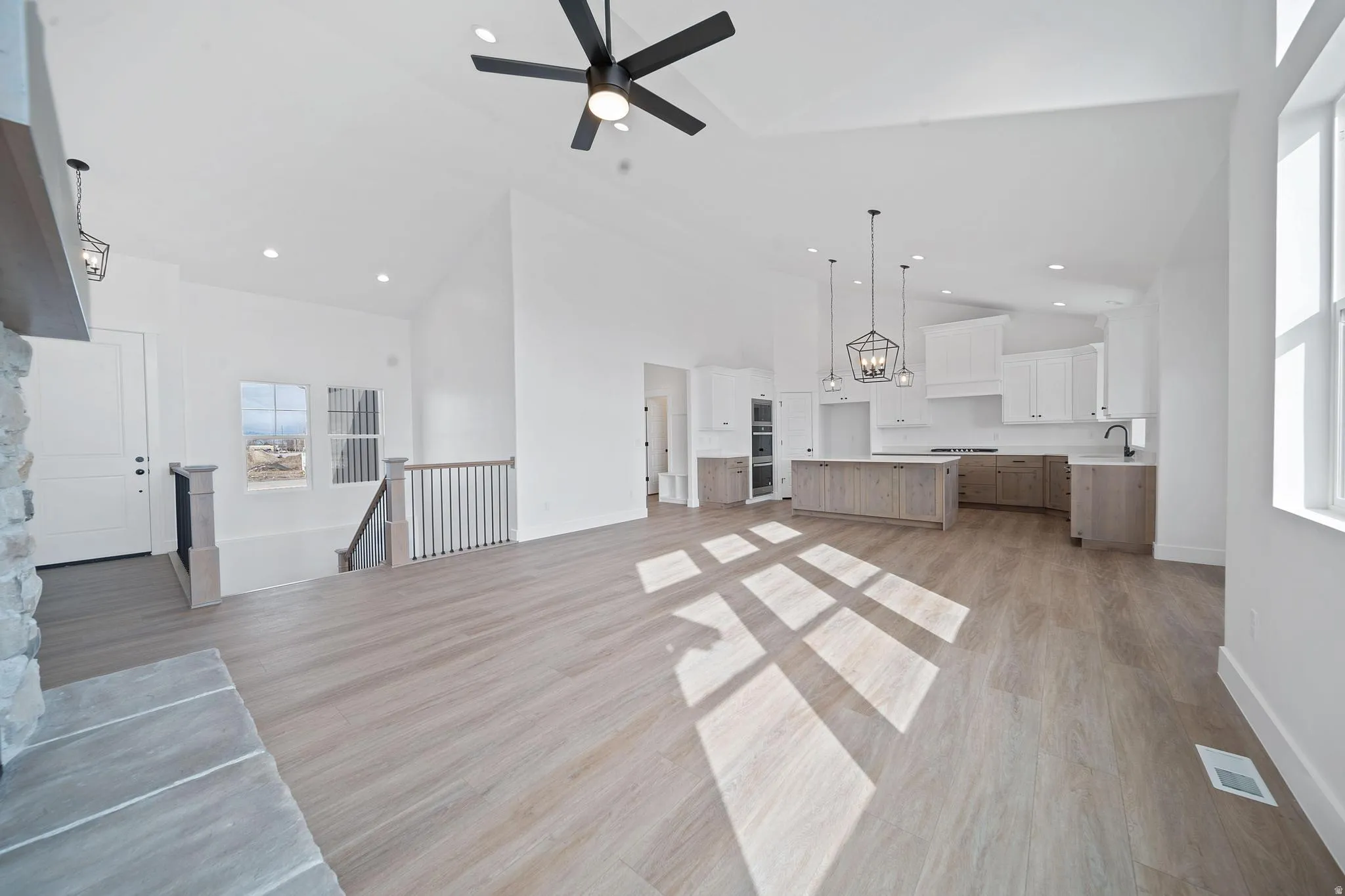 Unfurnished living room featuring light wood-style flooring, ceiling fan, a chandelier, and high vaulted ceiling