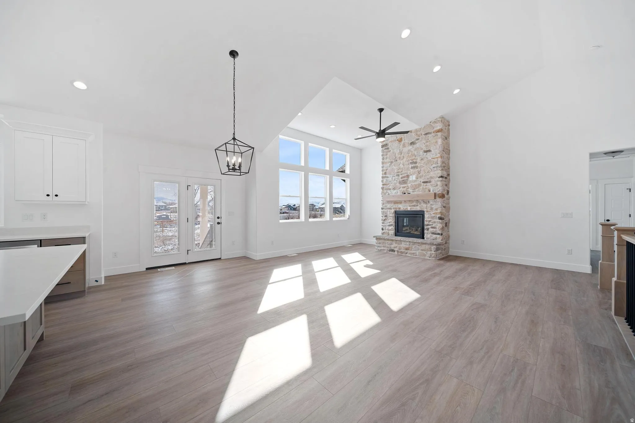 Unfurnished living room featuring high vaulted ceiling, a stone fireplace, a chandelier, light wood-style floors, and a ceiling fan