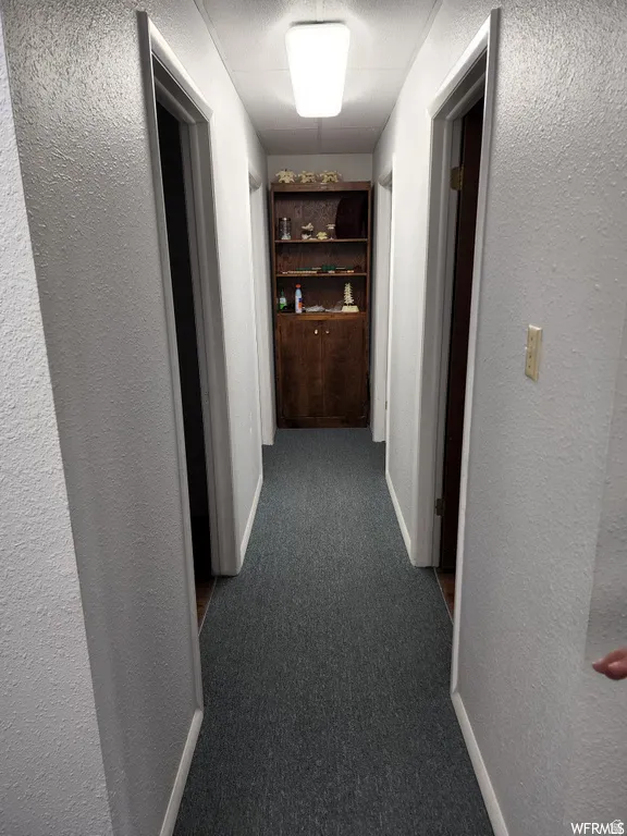 Hall featuring a textured wall, dark colored carpet, and a textured ceiling