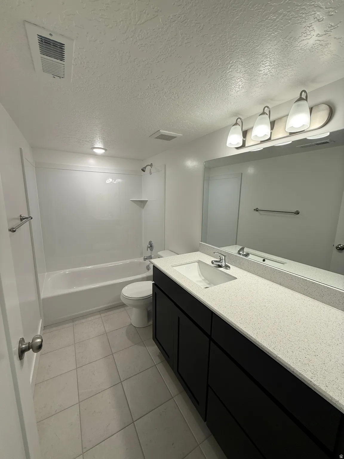 Bathroom with a textured ceiling, vanity, bathtub / shower combination, and light tile patterned floors