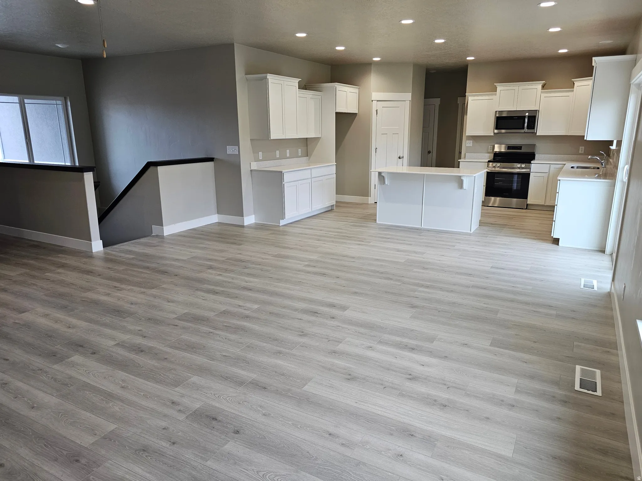 Kitchen with appliances with stainless steel finishes, recessed lighting, white cabinets, a center island, and a kitchen bar