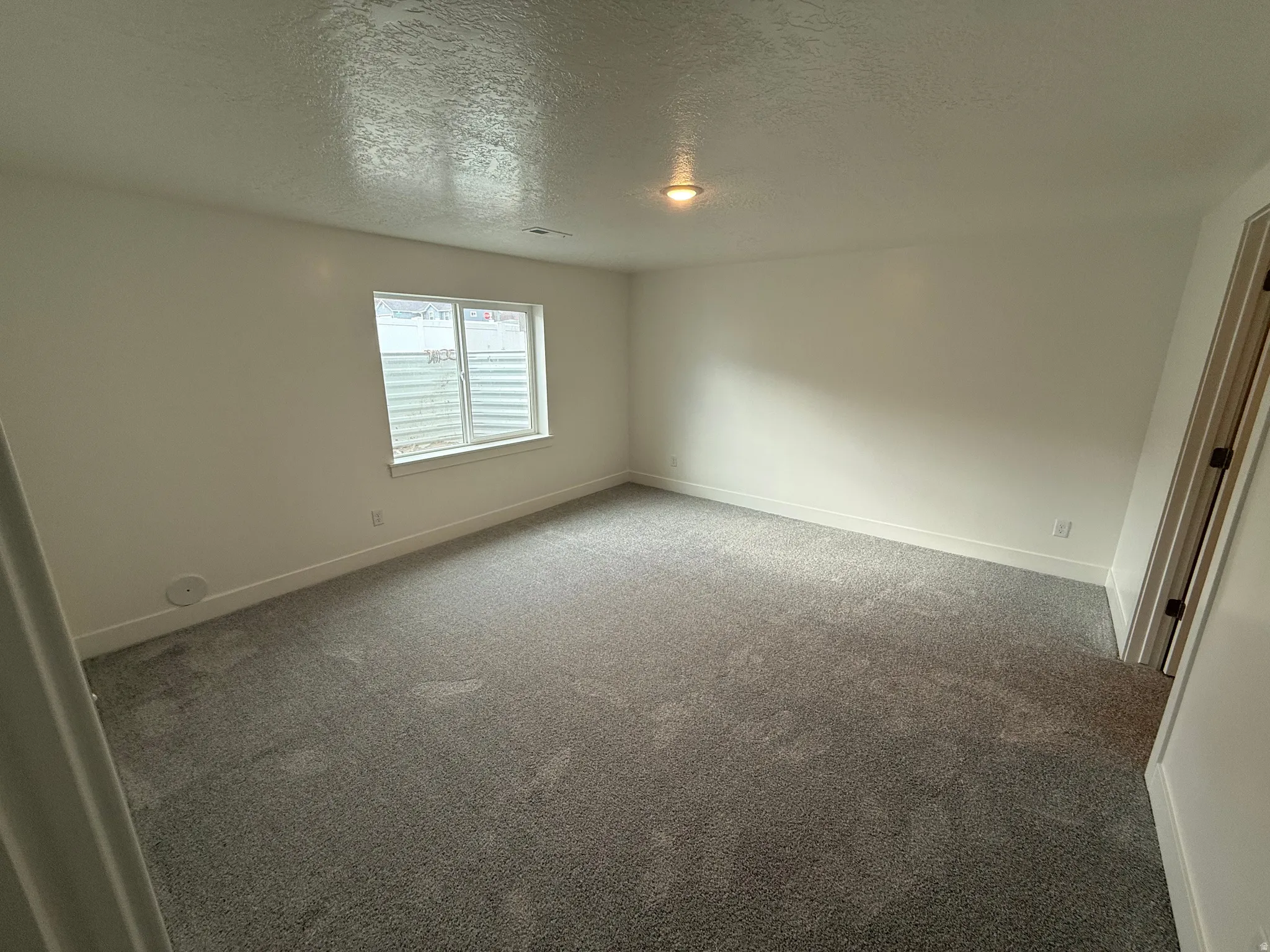Empty room with a textured ceiling and carpet flooring