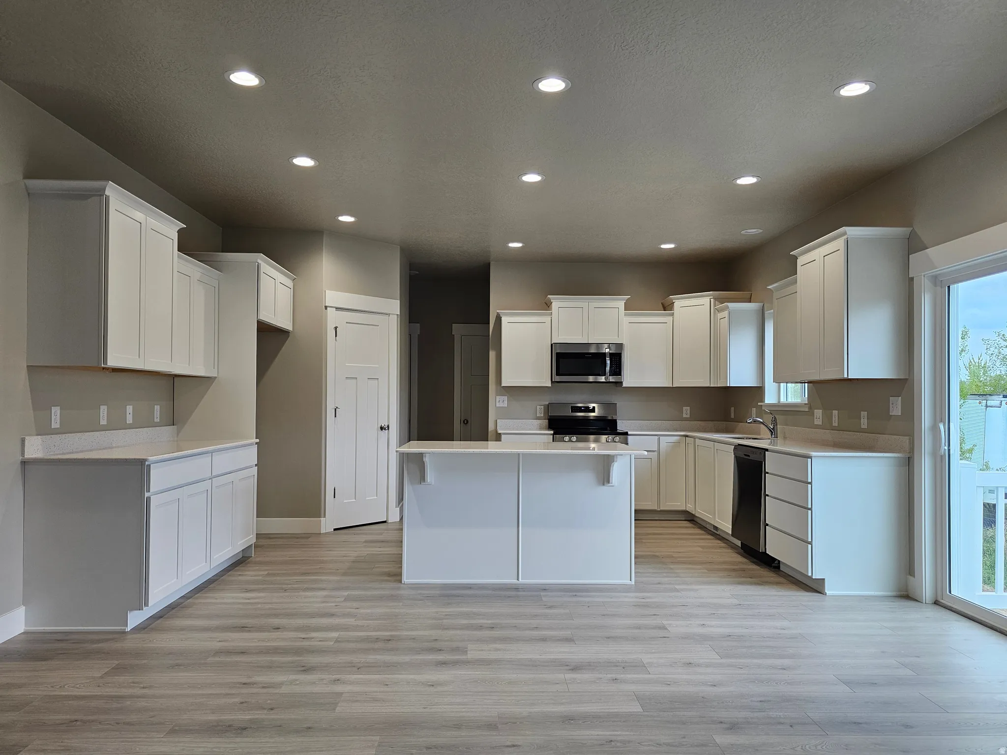 Kitchen with recessed lighting, white cabinetry, light wood-style floors, stainless steel appliances, and a center island
