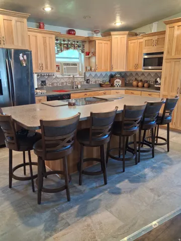 Expansive kitchen island with built-in cooktop, ample countertop space, extensive light wood cabinetry, recessed lighting, and tile flooring