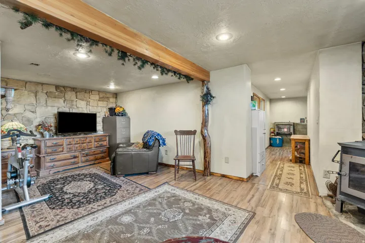 Living room with a wood stove, beam ceiling, light wood-style floors, recessed lighting, and a textured ceiling