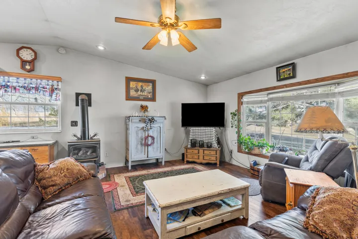 Living room featuring a wood stove, vaulted ceiling, dark wood-style flooring, ceiling fan, and recessed lighting