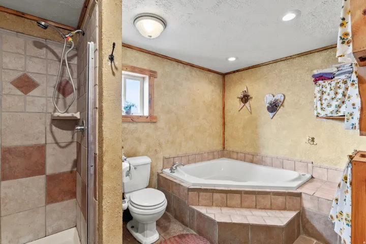 Bathroom featuring a stall shower, crown molding, a garden tub, a textured ceiling, and a textured wall