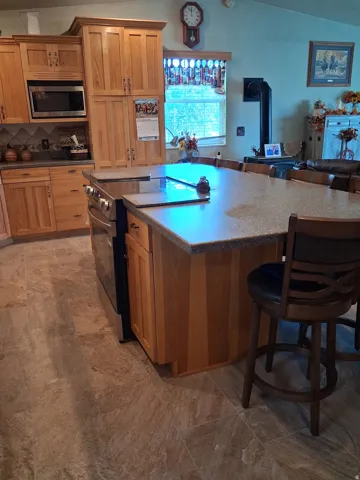Wood cabinetry, stainless steel microwave, tile backsplash, stone-finish countertops, and tile flooring