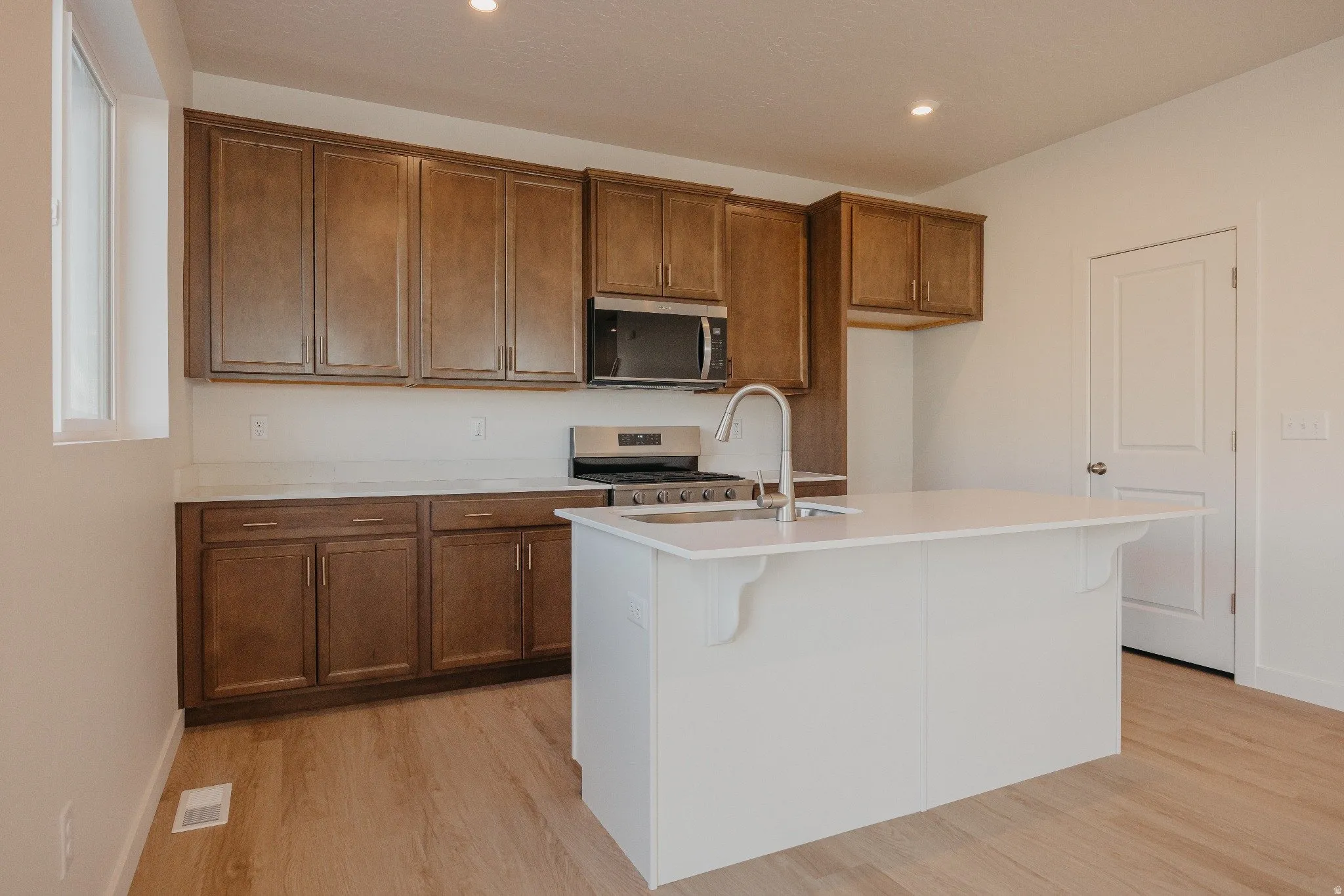 Kitchen with wood finish cabinetry, stainless steel appliances, a center island with sink, light wood-style floors, and recessed lighting