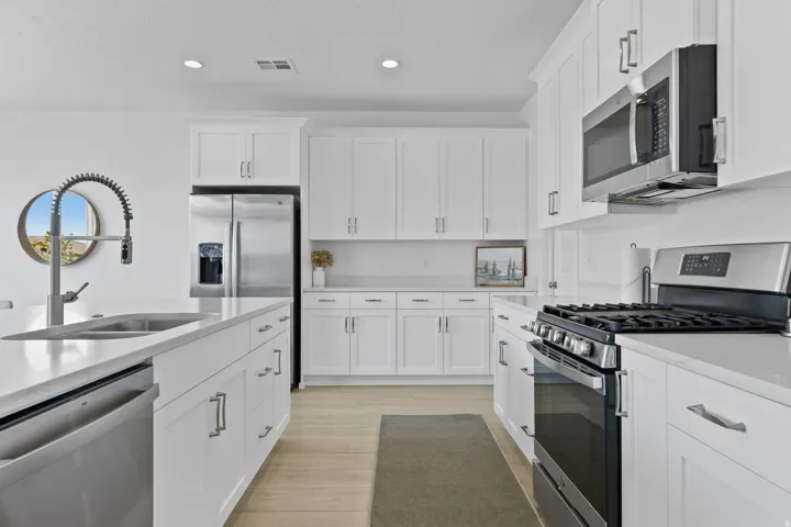 Kitchen with stainless steel appliances, recessed lighting, white cabinets, light stone counters, and light wood-style floors