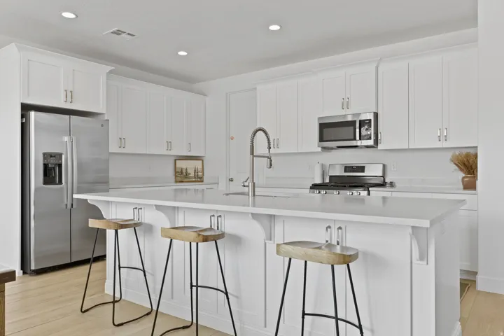 Kitchen with white cabinetry, appliances with stainless steel finishes, a kitchen bar, an island with sink, and light wood finished floors