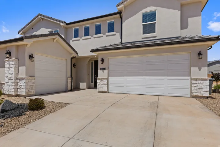 View of front of home with stone siding, concrete driveway, stucco siding, and an attached garage