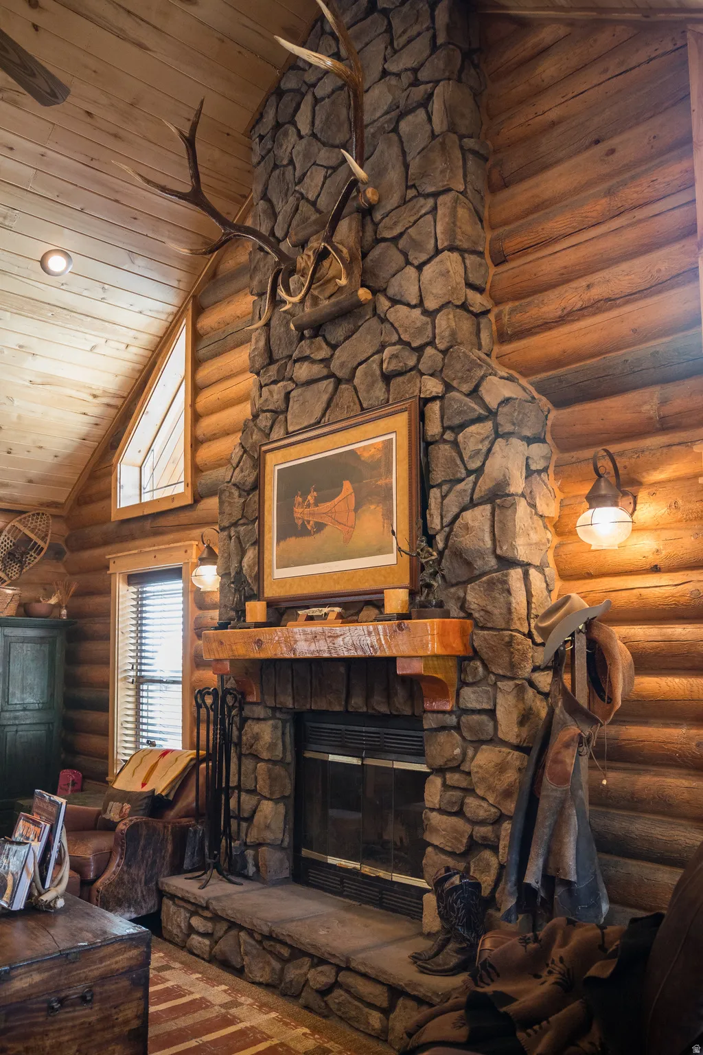 Living room featuring a stone fireplace, log walls, high vaulted ceiling, and wooden ceiling