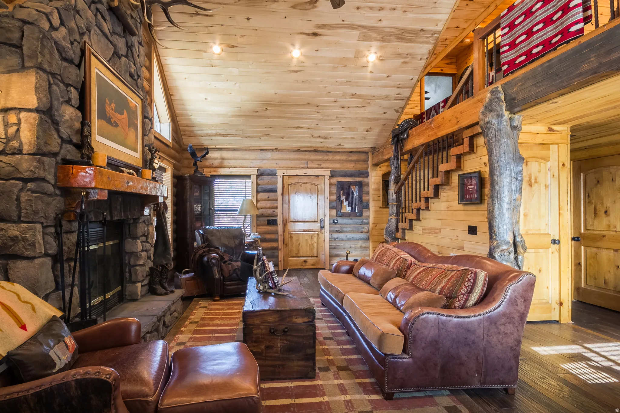 Living room featuring high vaulted ceiling, wooden ceiling, hardwood / wood-style floors, a stone fireplace, and stairway