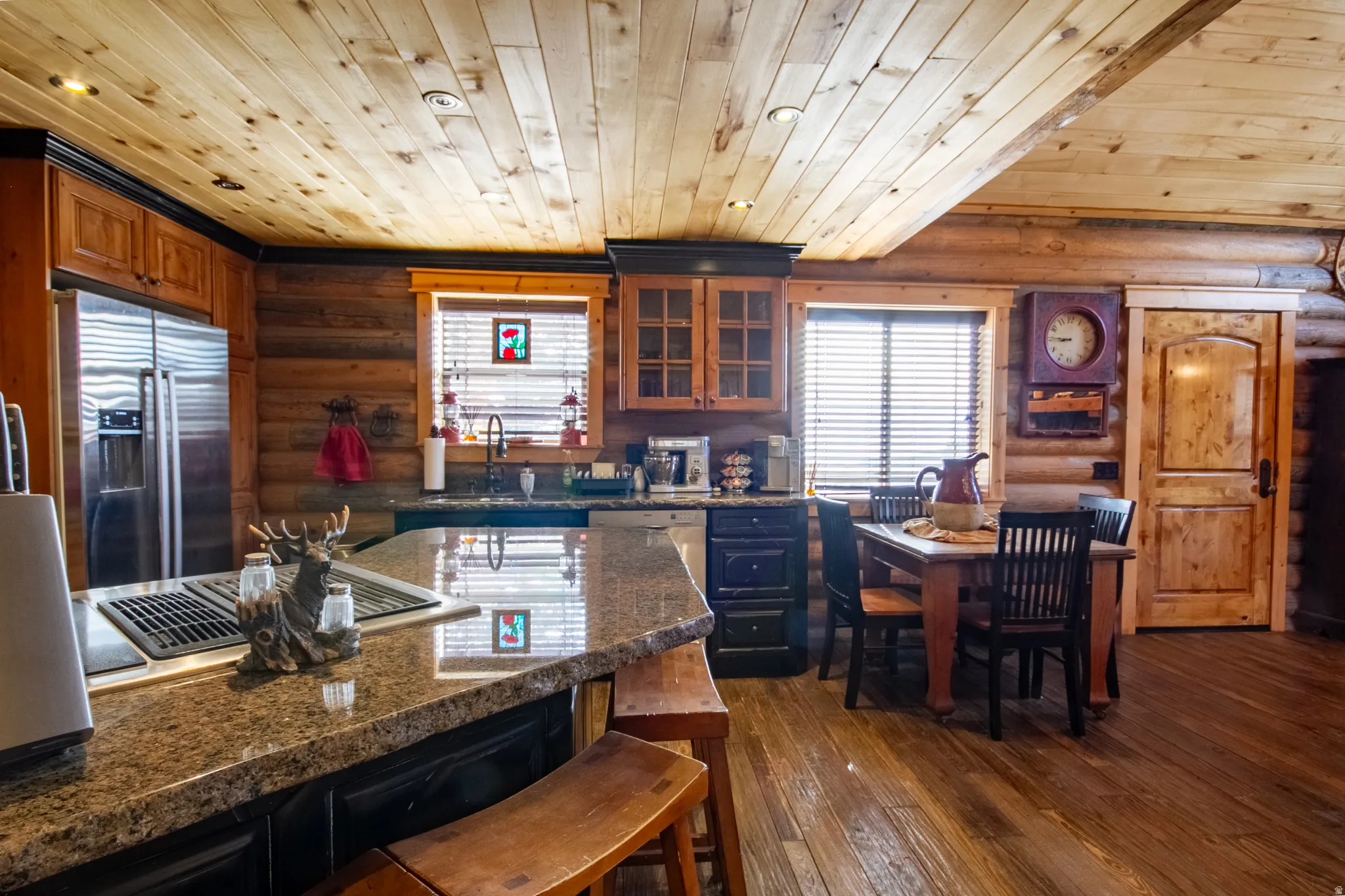 Kitchen with rustic walls, a kitchen breakfast bar, dark wood-style flooring, glass insert cabinets, and stainless steel appliances