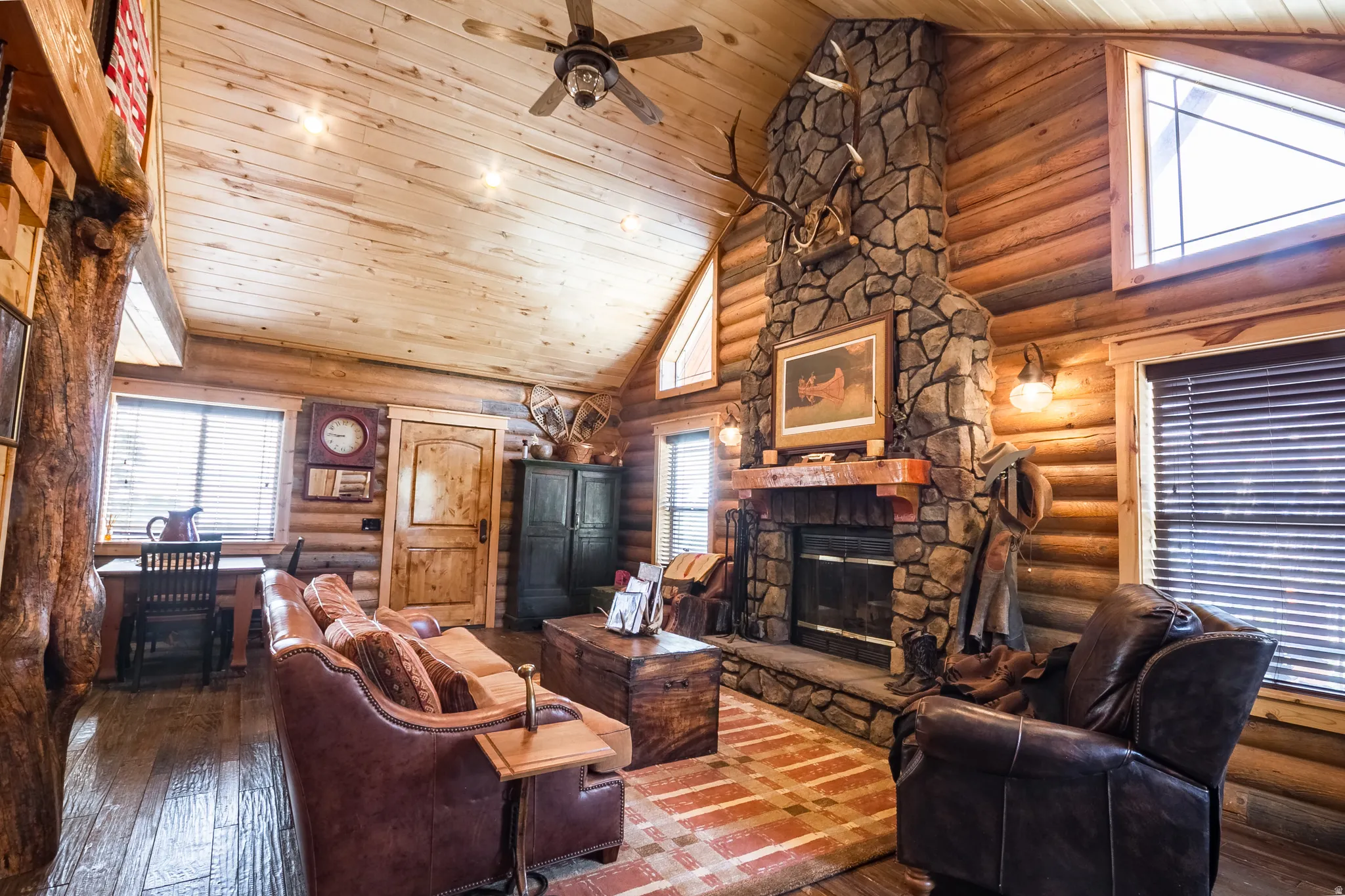 Living area with high vaulted ceiling, hardwood / wood-style flooring, a stone fireplace, wooden ceiling, and log walls