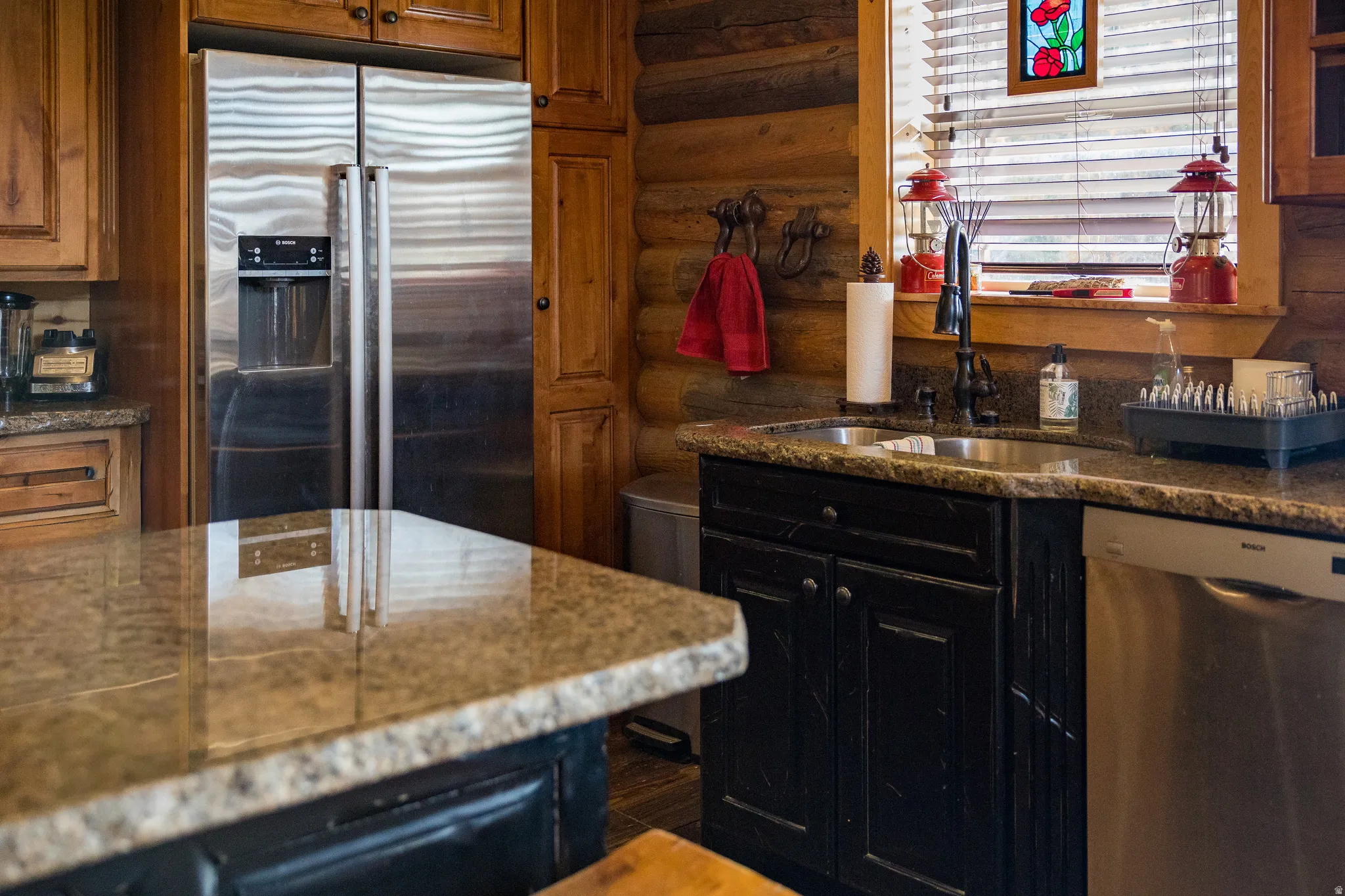 Kitchen with stainless steel appliances, log walls, dark cabinets, dark stone counters, and brown cabinets