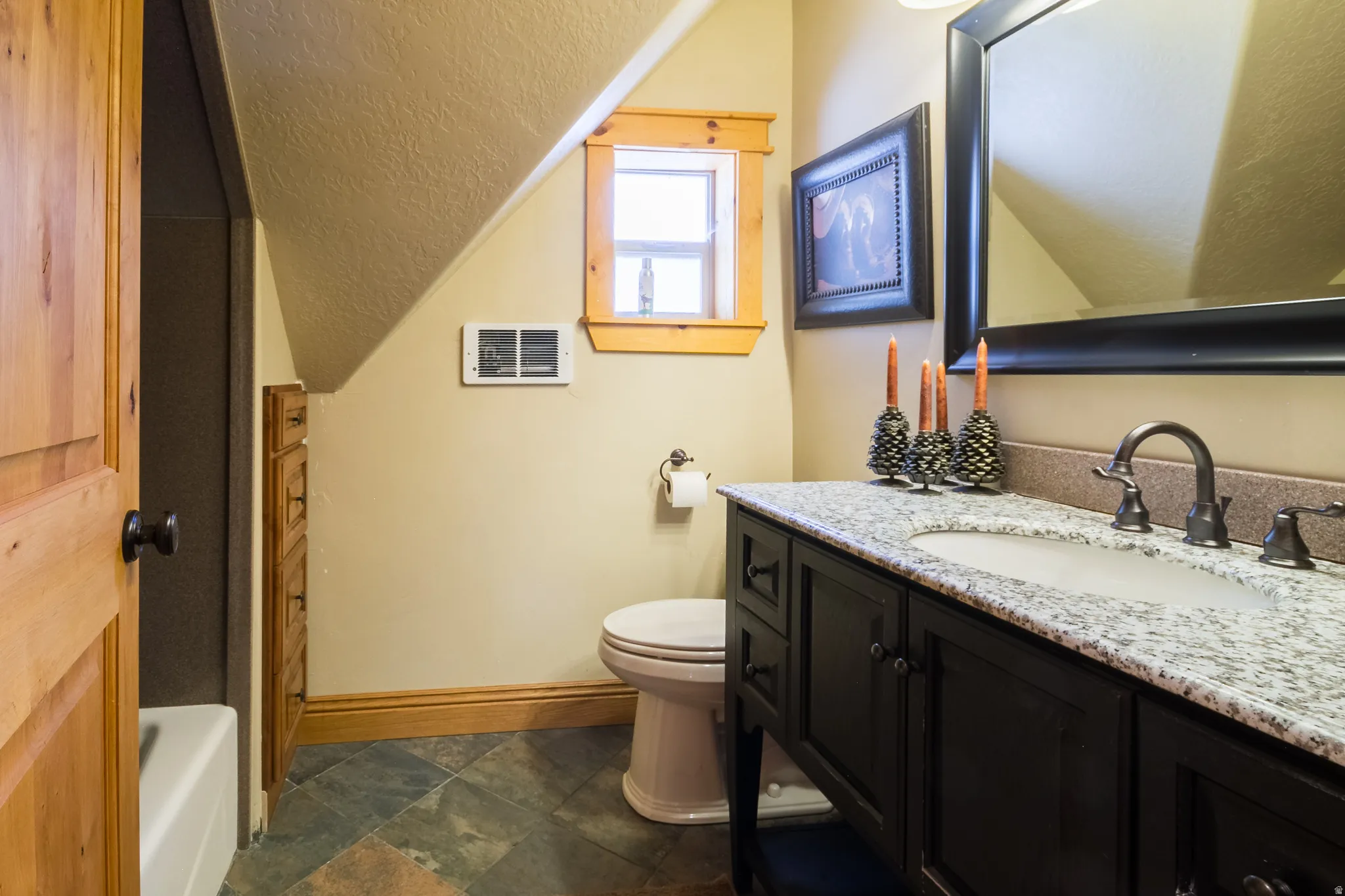 Full bath with vanity, a textured ceiling, dark stone finish floors, vaulted ceiling, and a tub