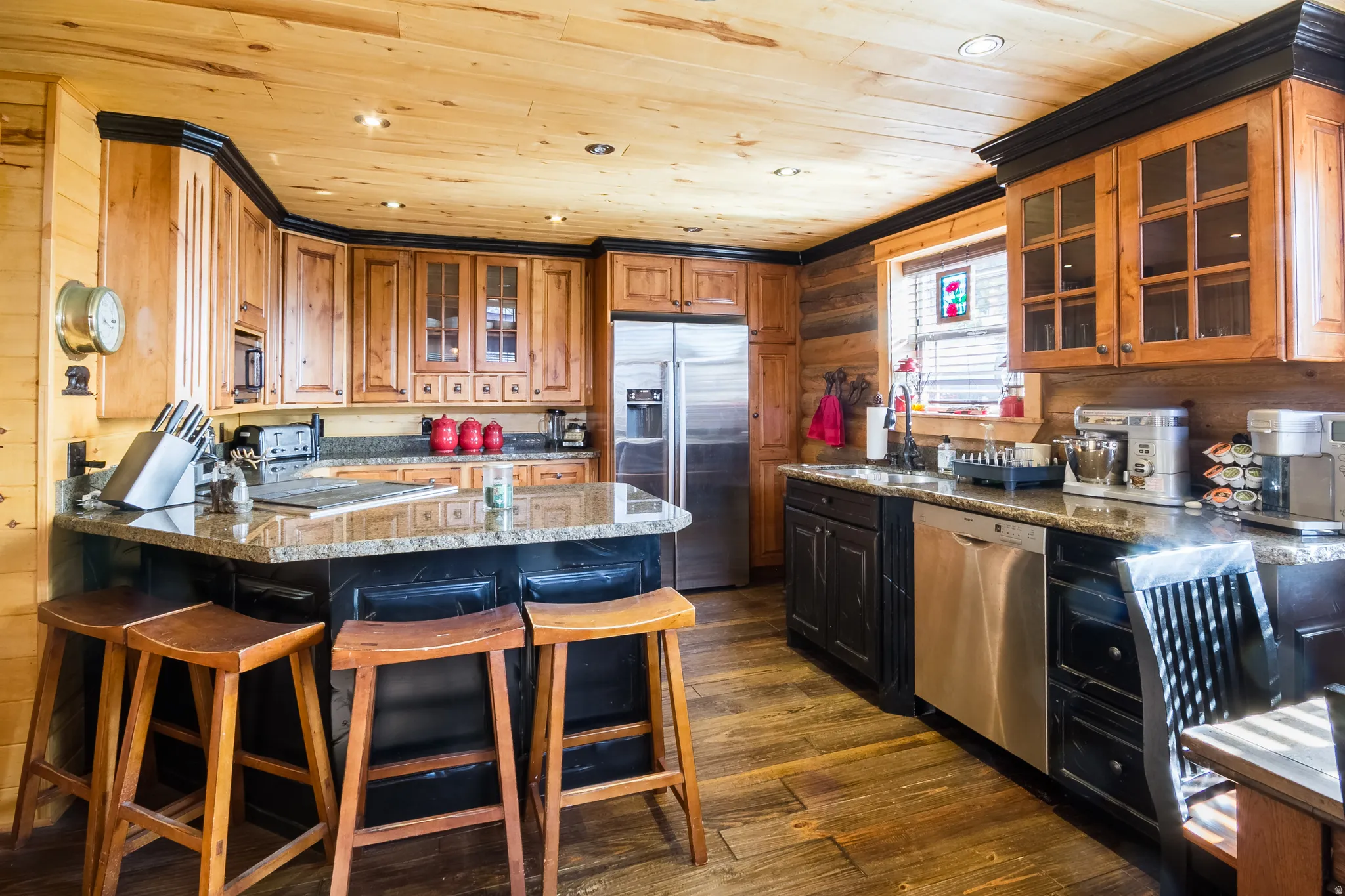 Kitchen with glass insert cabinets, wooden walls, a kitchen breakfast bar, stainless steel appliances, and dark wood-style floors