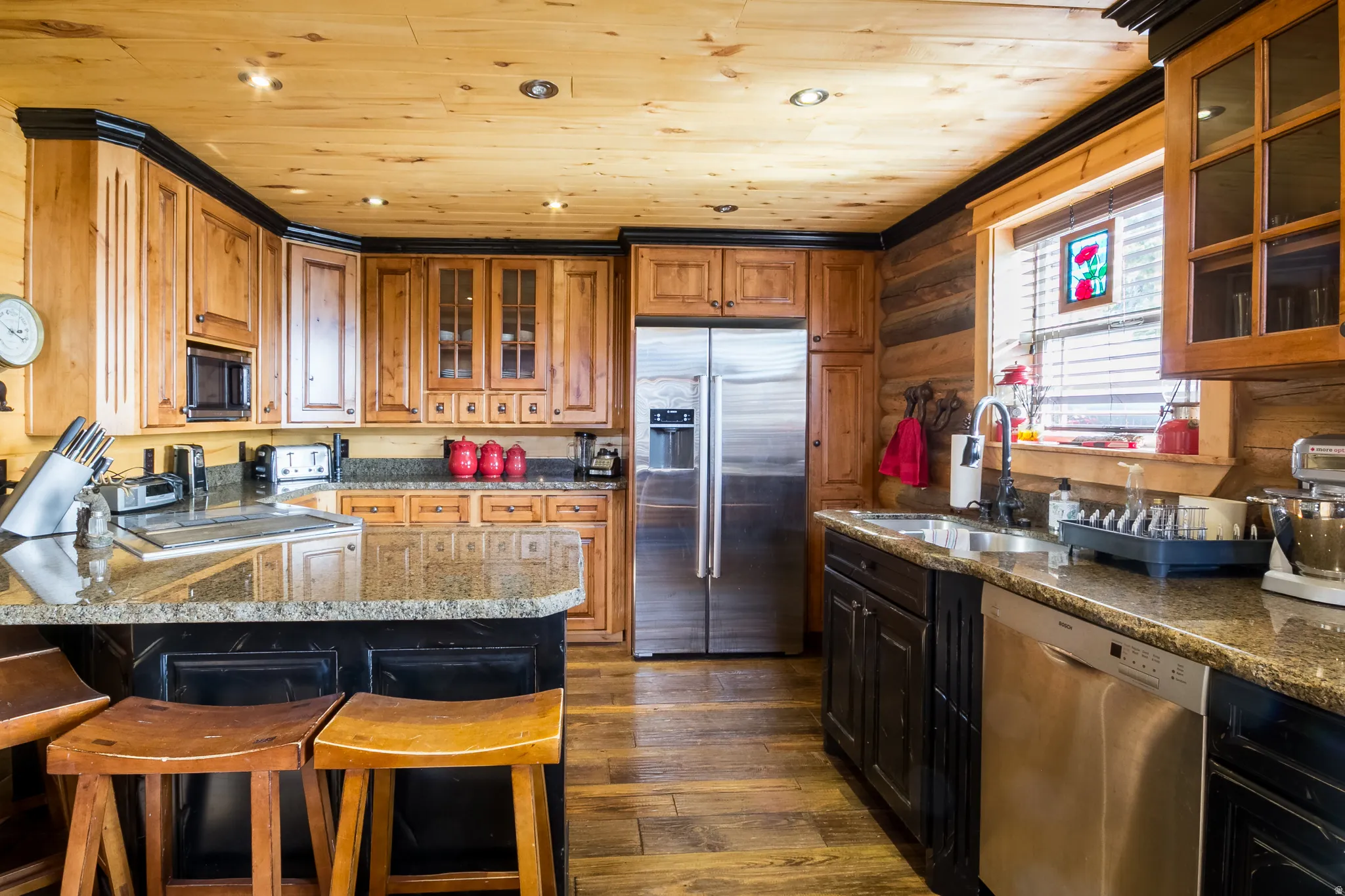 Kitchen with glass insert cabinets, appliances with stainless steel finishes, dark wood-style flooring, a breakfast bar, and brown cabinets