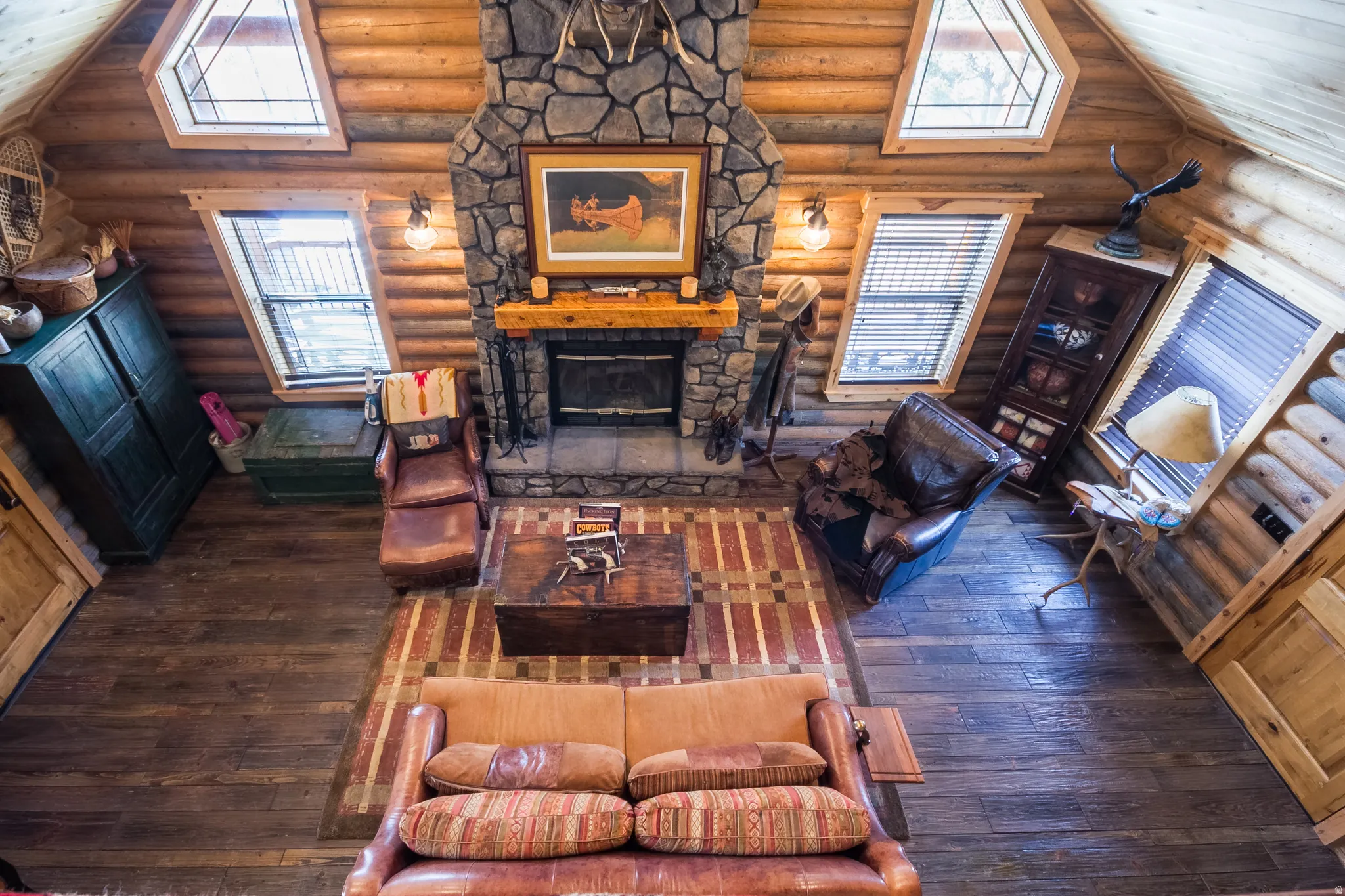 Living room with dark wood-style floors, vaulted ceiling, a stone fireplace, and rustic walls