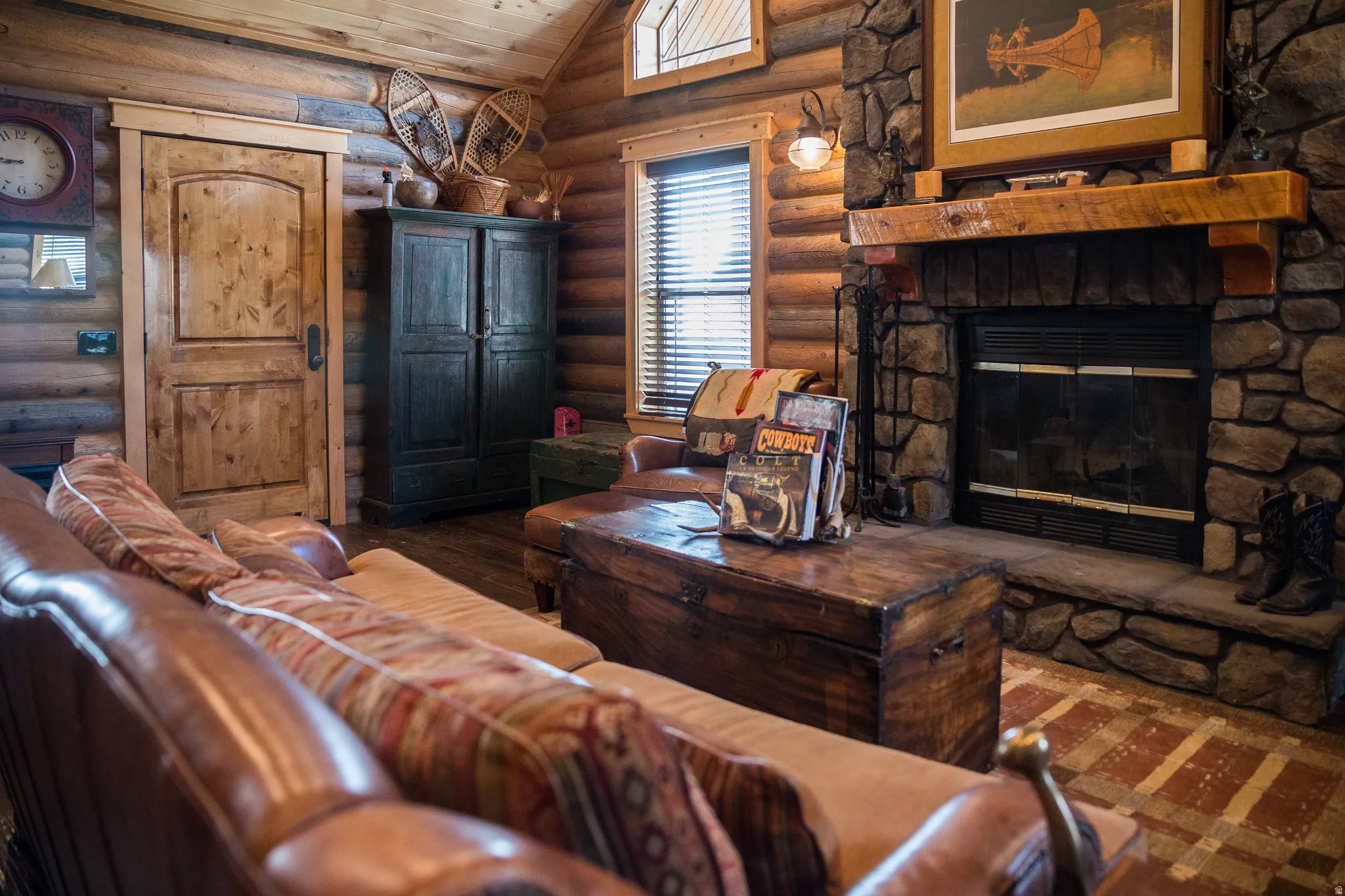 Living area with vaulted ceiling, a stone fireplace, log walls, dark wood-style flooring, and wooden ceiling