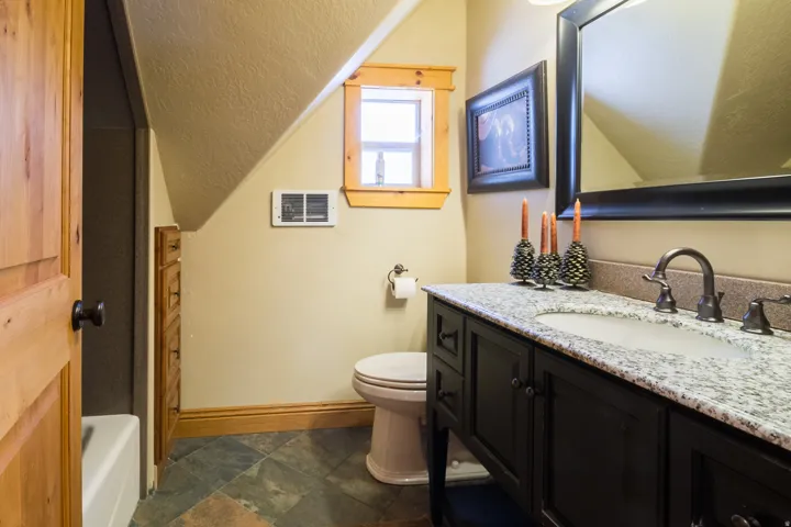 Full bath with vanity, a textured ceiling, dark stone finish floors, vaulted ceiling, and a tub