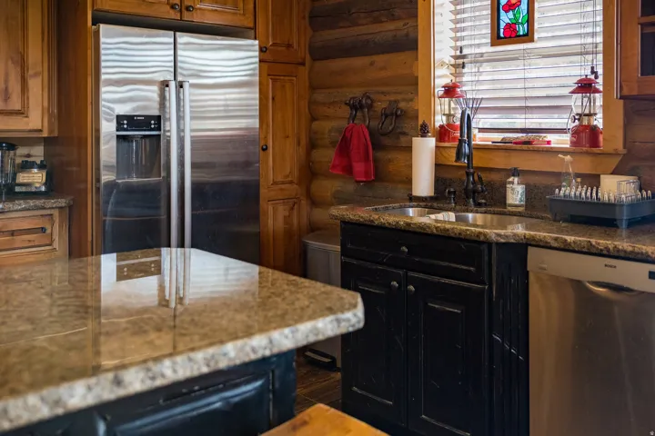 Kitchen with stainless steel appliances, log walls, dark cabinets, dark stone counters, and brown cabinets