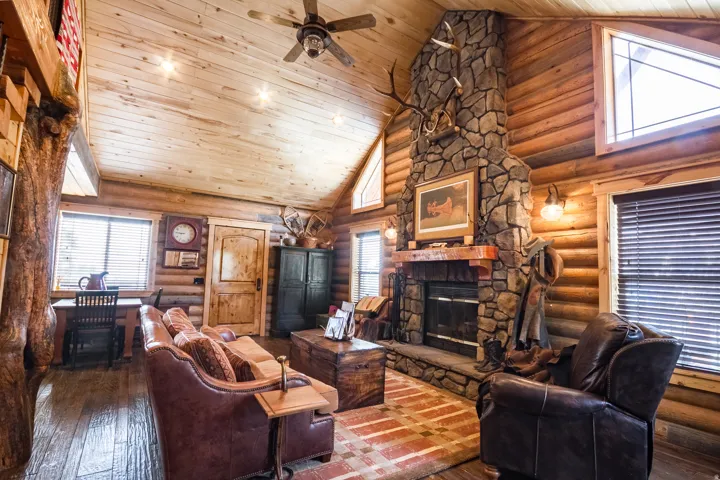 Living area with high vaulted ceiling, hardwood / wood-style flooring, a stone fireplace, wooden ceiling, and log walls