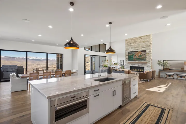 Kitchen featuring open floor plan, a stone fireplace, light stone counters, dark wood-style floors, and an island with sink