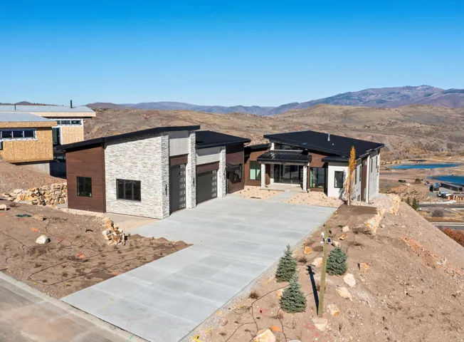 View of front facade featuring stone siding, a mountain view, driveway, a patio, and an attached garage