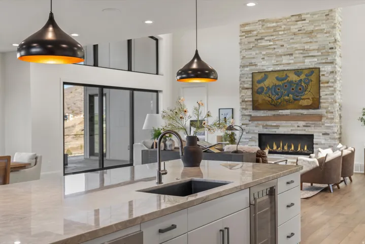 Kitchen with white cabinetry, light stone counters, a stone fireplace, open floor plan, and a high ceiling