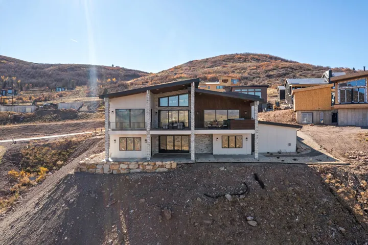 Back of property with a mountain view, a balcony, a patio, and stone siding