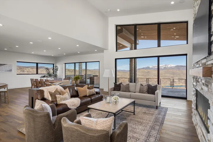 Living room with a high ceiling, a stone fireplace, dark wood-style floors, and recessed lighting