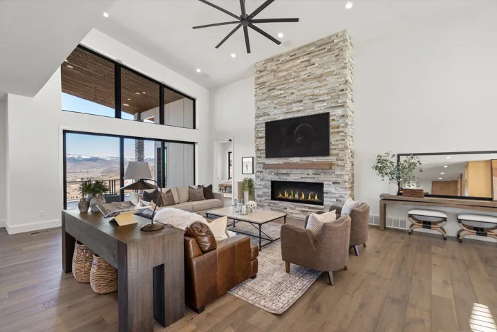 Living area with wood-type flooring, a high ceiling, a stone fireplace, a ceiling fan, and recessed lighting
